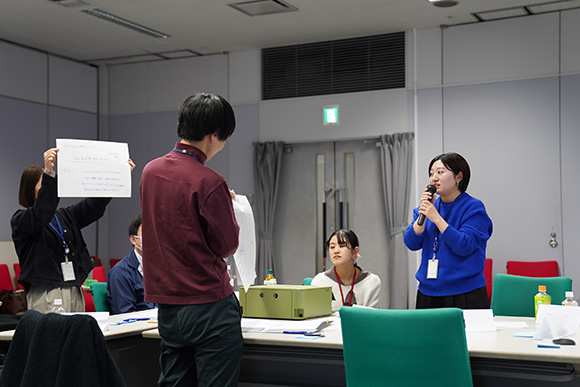 前方に紙を掲げている人とマイクをもって話をしている人